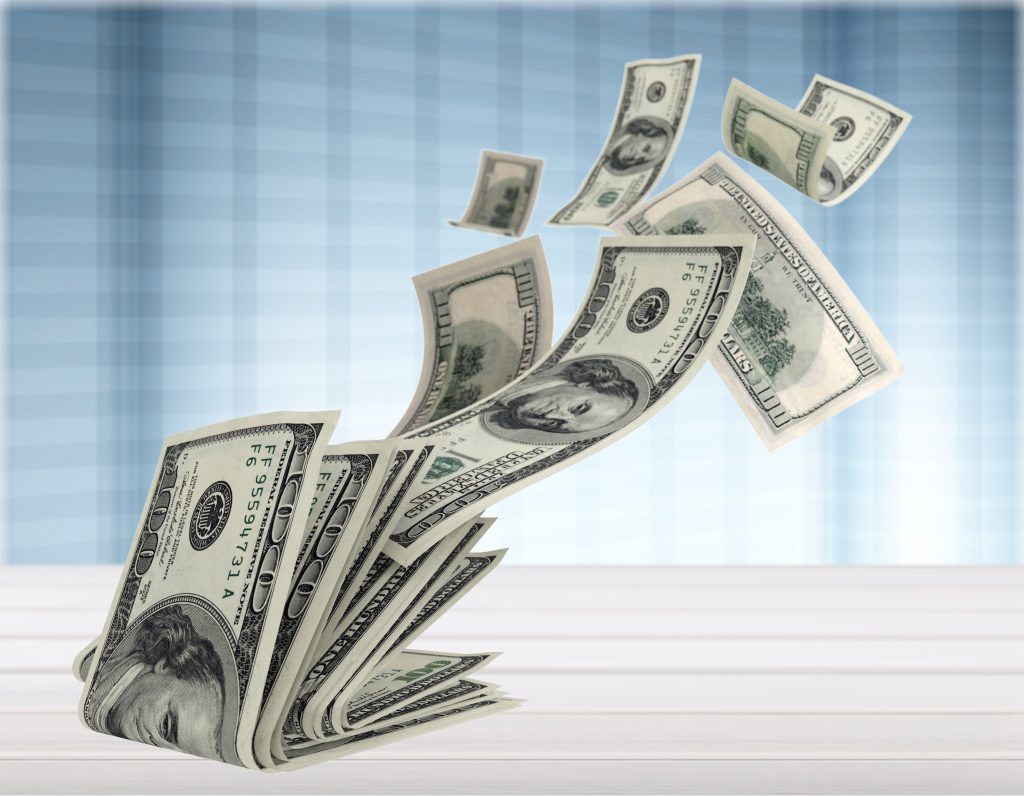Header image: sheaf of $100 bills on a table, with more bills flying away (Credit: Billion Photos / Shutterstock.com)