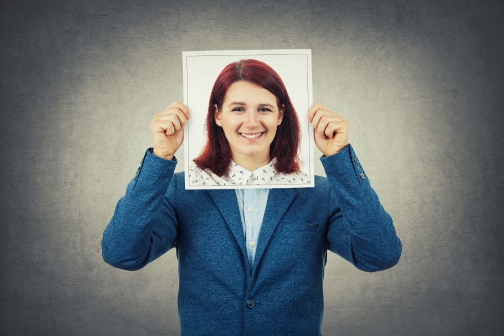 Header image: man holding image of woman's face in front of his face as a disguise (credit: StunningArt / Shutterstock.com)