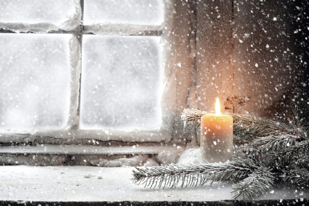 Header image: candle buring on snowy windowsill amid evergreen boughs