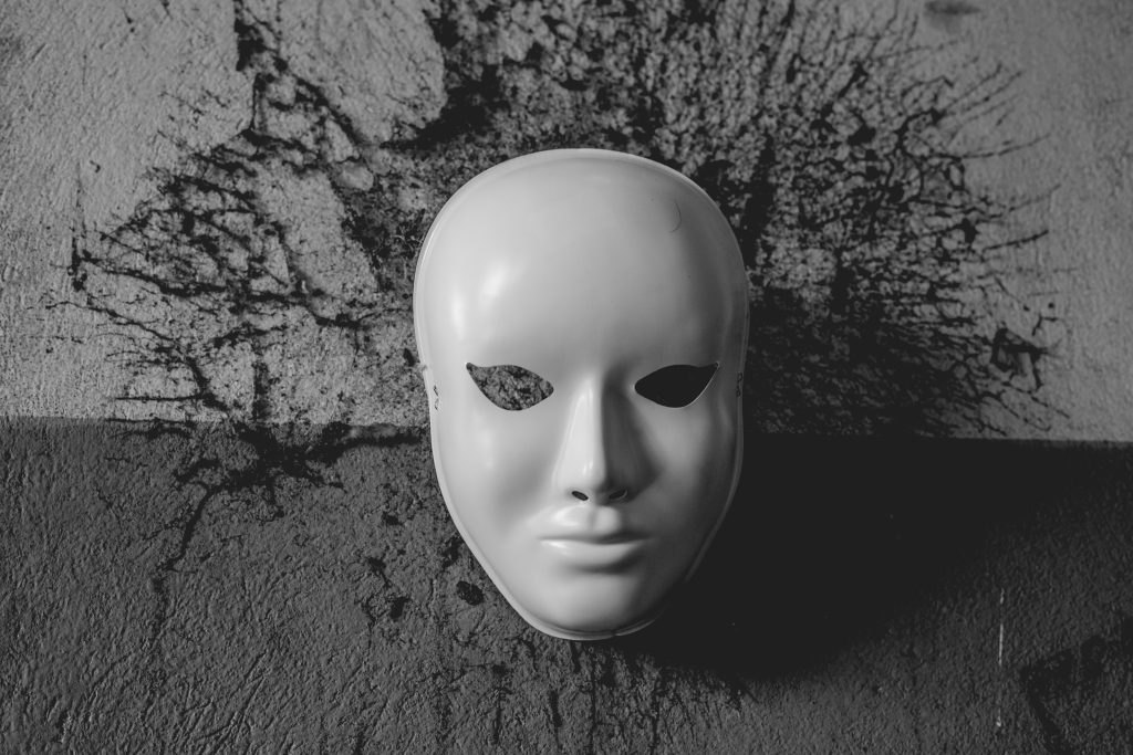 Header image: white full-face mask lying on a textured gray background, surrounded by a black splatter-pattern halo (Credit: Photo by Edilson Borges on Unsplash.com)