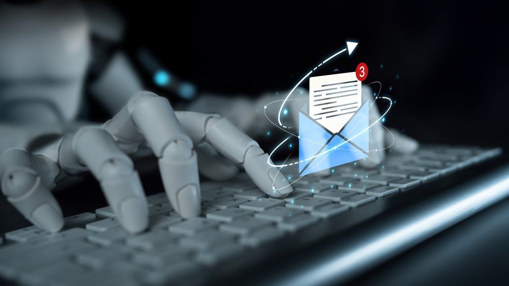 Header image: white robot fingers typing on a gray keyboard against black background. Above the keyboard hovers a visualization of an email message: a document halfway inside a mailing envelope (Credit: Koupei Studio / Shutterstock.com)
